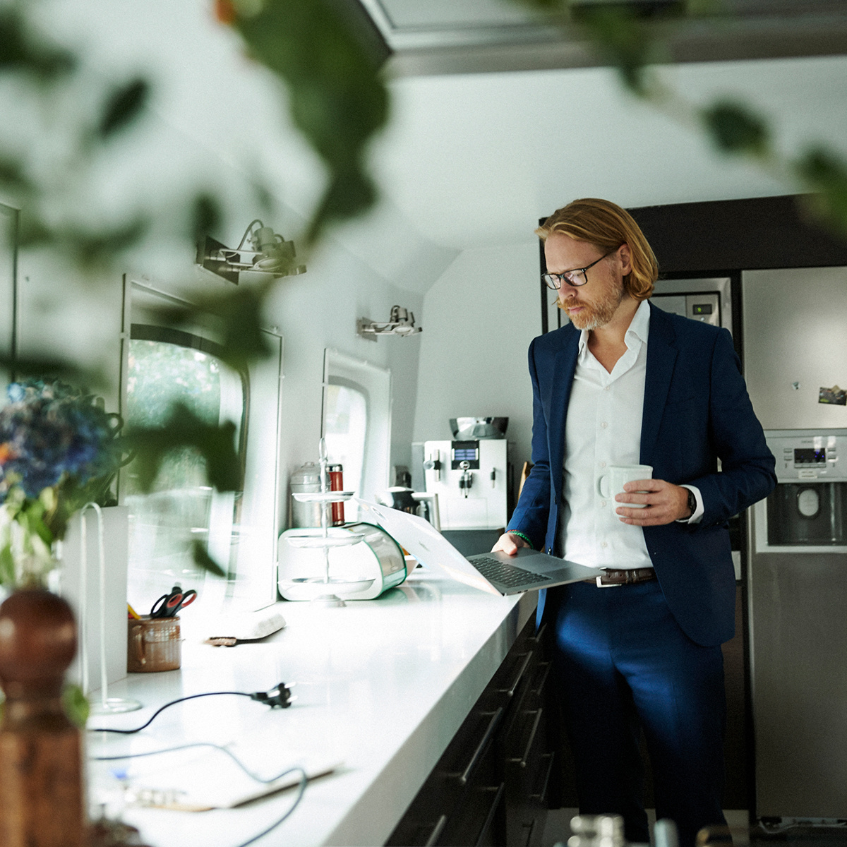 En person som står vid en köksbänk med en kaffekopp i handen och har en laptop framför sig | Min Inköpsavdelning - Seiva.